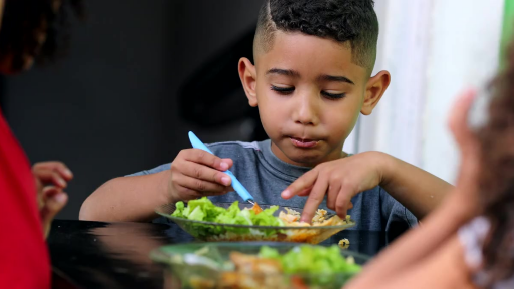 Young boy sits at a table eating a salad with a fork.
Caring Gift of Food