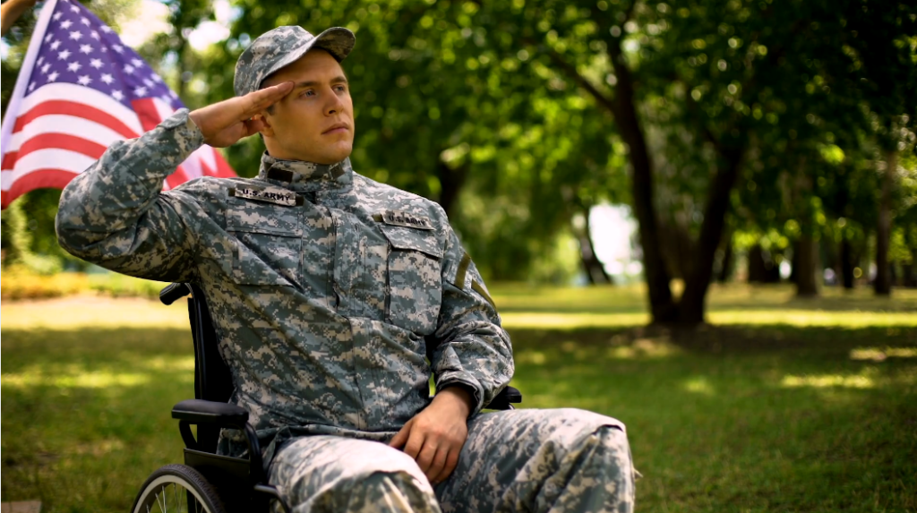 Man in a military uniform sits in a wheelchair outside saluting a waving American flag.
Caring Gift of Honor