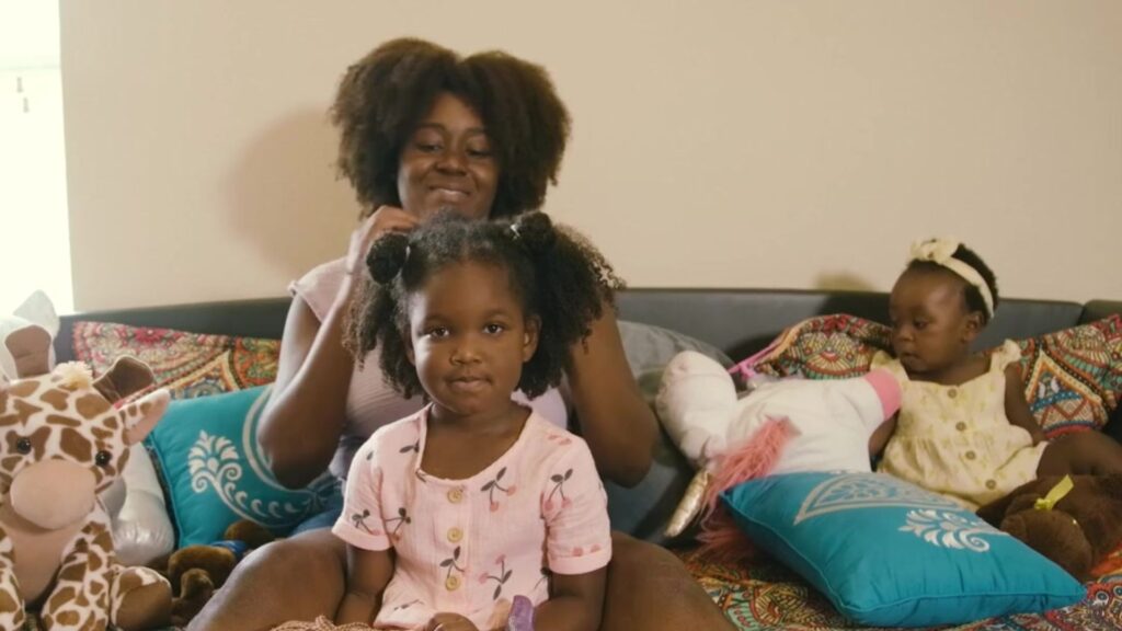 A smiling mother fixes her daughters hair on a couch while her younger daughter plays next to them.
Caring Gift of Shelter