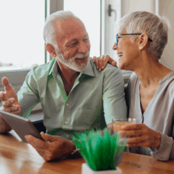 Older couple with tablet, looking at each other smiling.