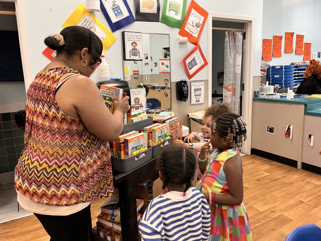 teacher hands out books to pre-school age children