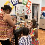 teacher hands out books to pre-school age children