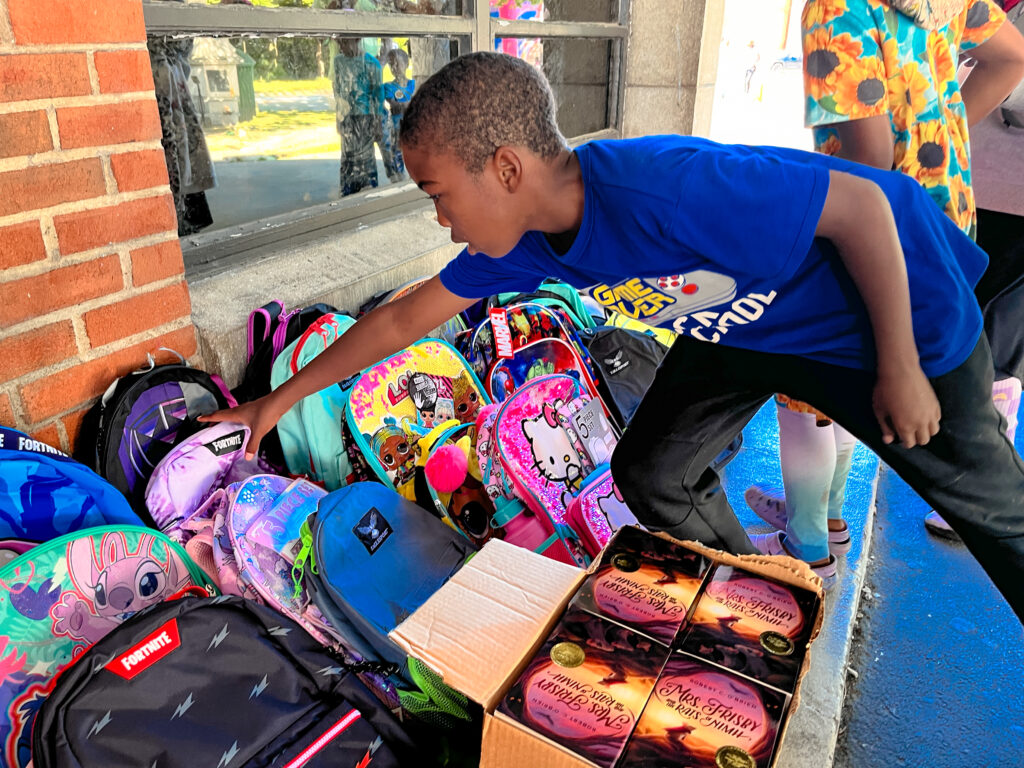 Young kid reaches for a backpack in a pile of backpacks.
