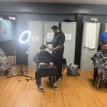Three men sit in barber chairs getting their hair cut.