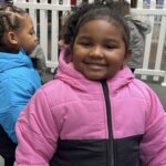 Pre-school age girl smiles as she wears her brand new pink and black winter coat.