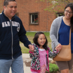 Father and mother hold hands with daughter as they walk
