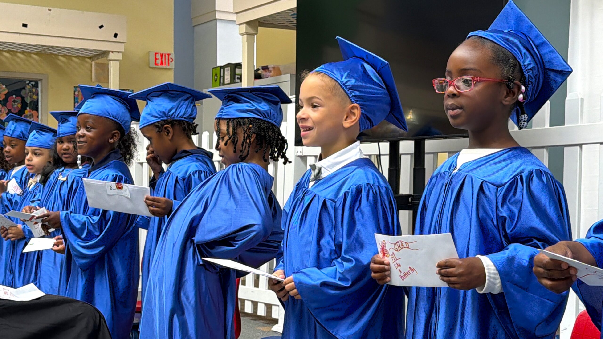 Smiling preschool children at the VOACC wearing blue graduation cap and gowns.