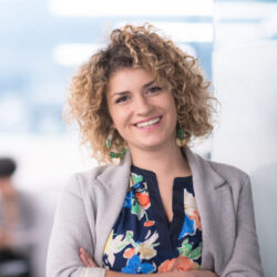 Woman with curly hair stands confidently and smiles